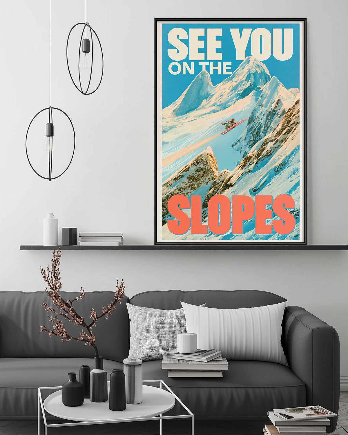 a poster of a mountain slope with a skier, hanging on a wall above a gray couch with a coffee table in front of it.