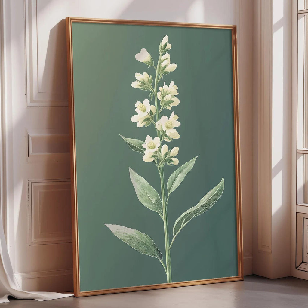 A framed print of a white flower with green leaves is displayed on a wall in a room with a window.