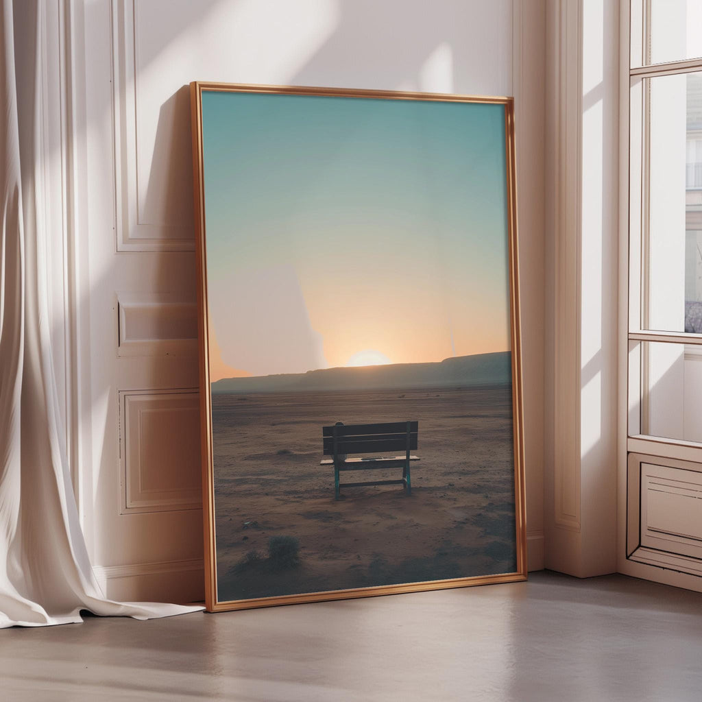 A large framed picture depicting a serene desert landscape at sunset, with a solitary bench in the foreground.