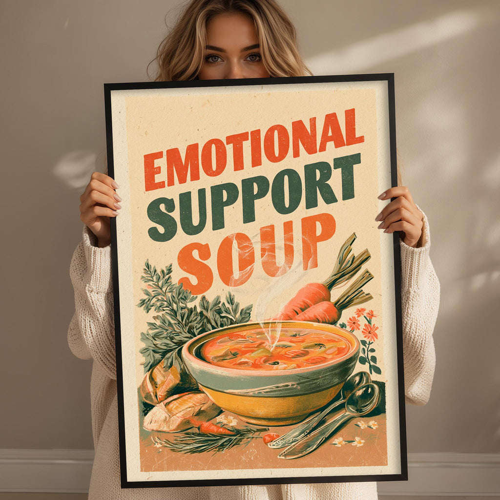 A woman holding a framed poster with the text "Emotional Support Soup" and an illustration of a bowl of soup.