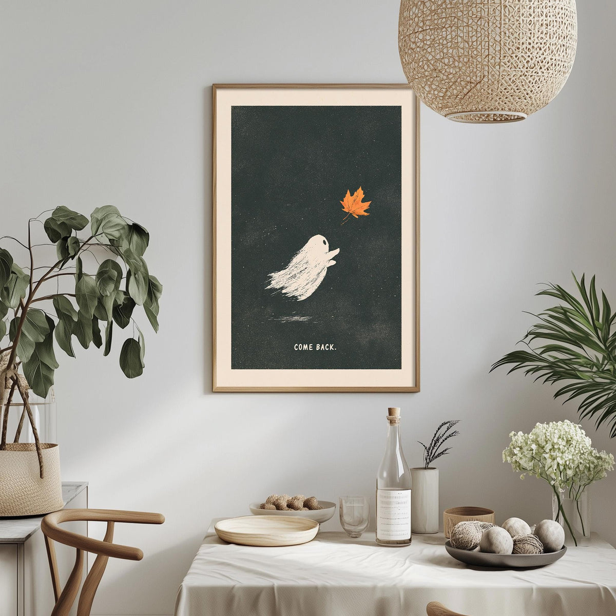 a framed poster of a ghost floating in the air, with a leaf in its mouth, hanging on a wall above a table with various items on it.