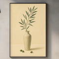 a kitchen counter with a framed picture of an olive branch and a vase of green leaves, along with various kitchen items such as a cutting board, a soap dispenser, and a bottle.