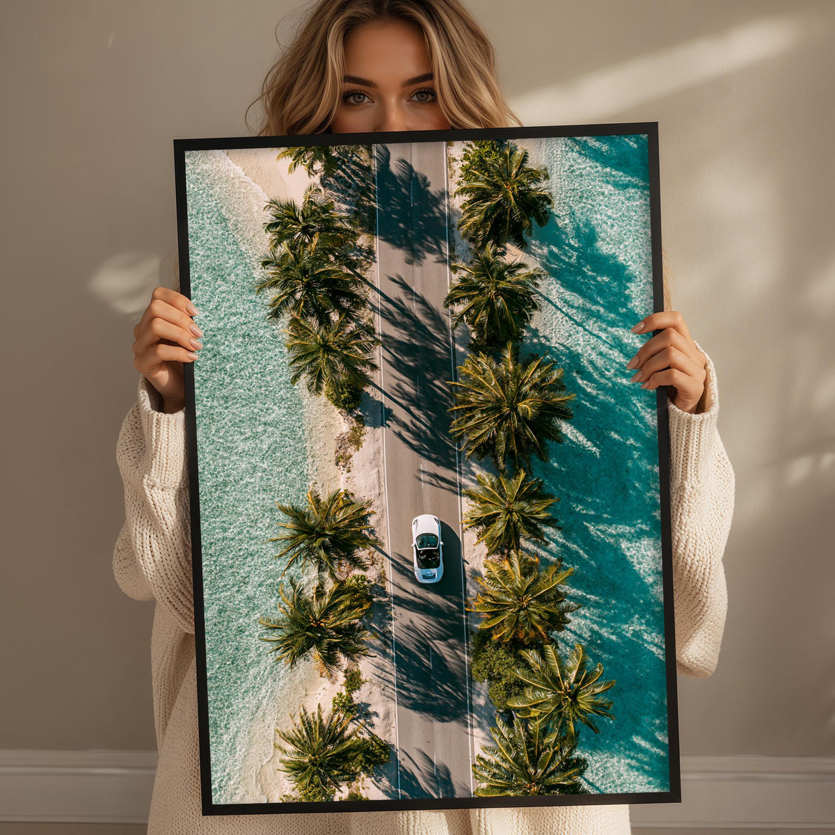 A woman holds up a framed image depicting a road lined with palm trees, with a car driving down the road.