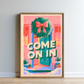 The image is a framed poster with a colorful, festive design featuring a wreath, presents, and a message that says "COME ON IN".