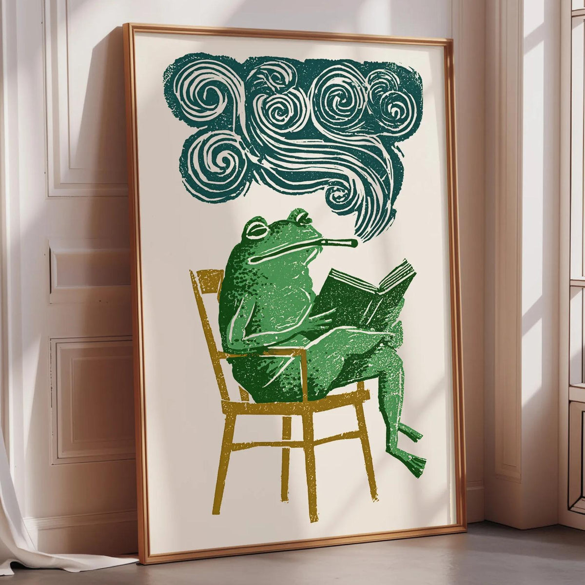 a framed illustration of a green frog sitting in a chair and reading a book, with a cloud-like shape above the frog.