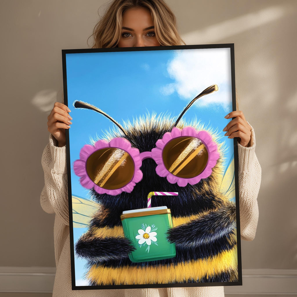 A woman holds up a framed picture of a bee wearing sunglasses and holding a drink.