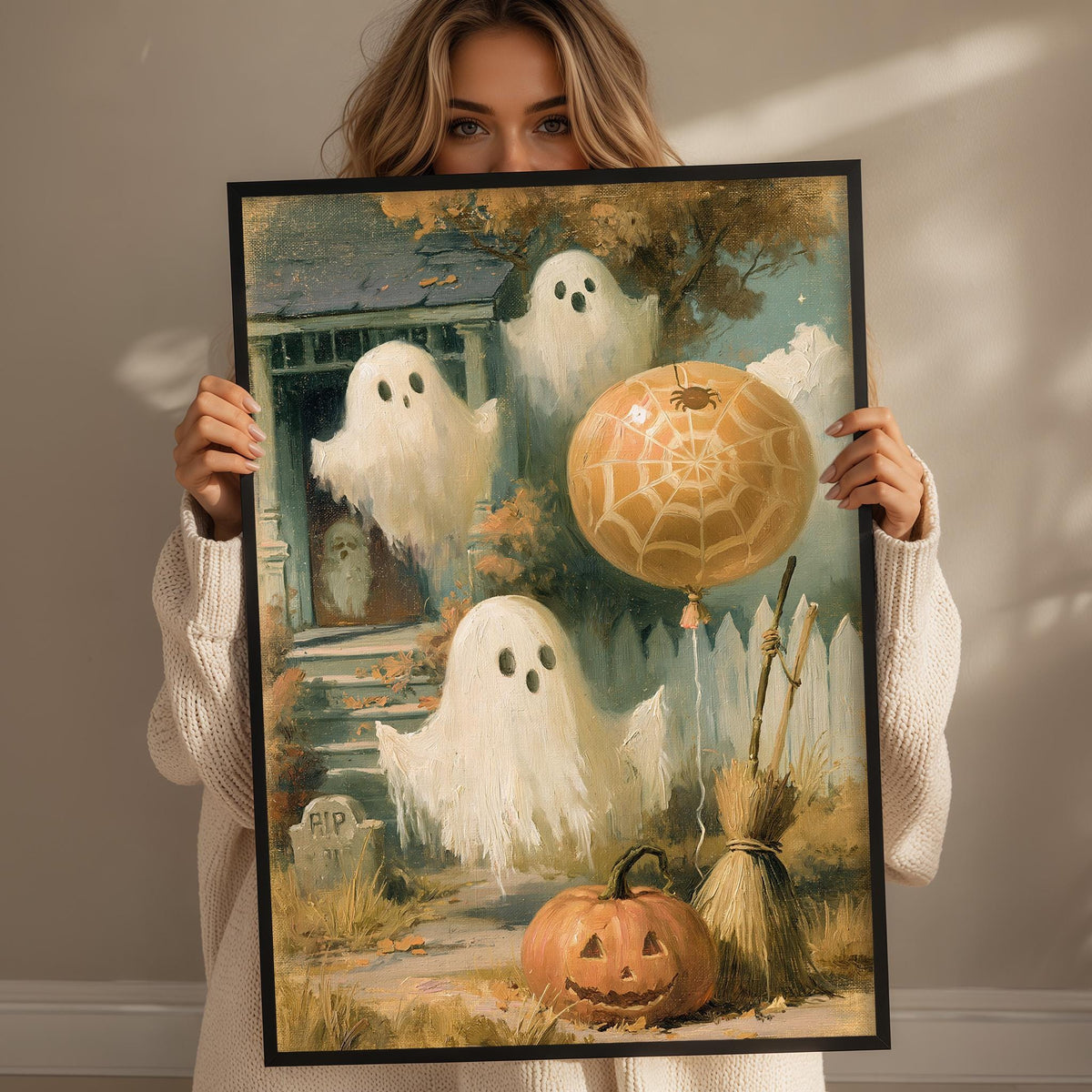 A woman holds up a framed painting depicting a Halloween scene with ghostly figures, a spider web, a pumpkin, and a broomstick.