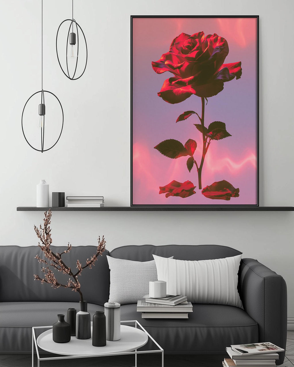 a large, vibrant red rose in a black frame, displayed on a wall above a gray couch with white pillows. The room has a minimalist and modern design, with a white coffee table, pendant lights, and a shelf with decorative items.