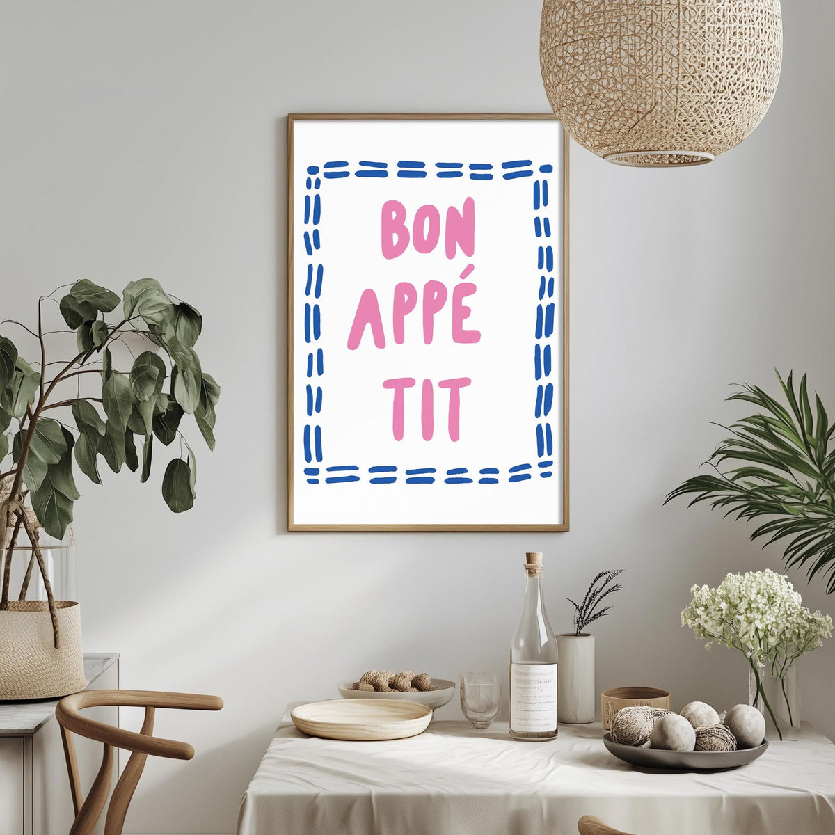 a dining table with a bowl of fruit, a bottle, and a vase of flowers, along with a framed poster with the text " bon appe tit" hanging on the wall above the table.