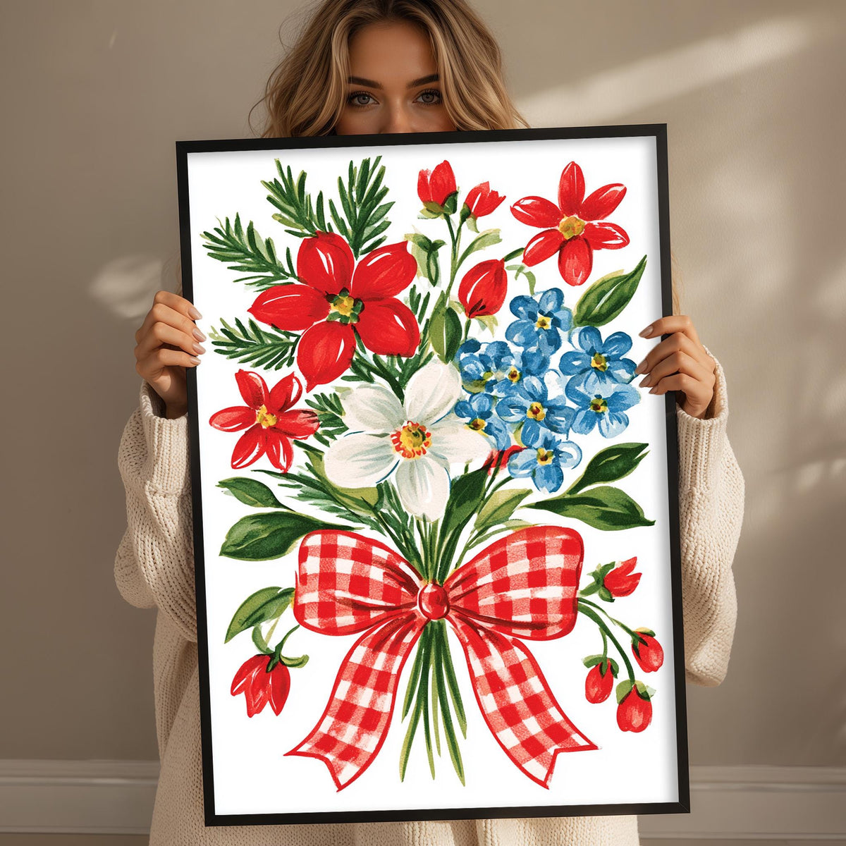 A woman is holding up a framed print of a vibrant floral arrangement, featuring red, white, and blue flowers, along with green leaves and a red and white checkered bow.