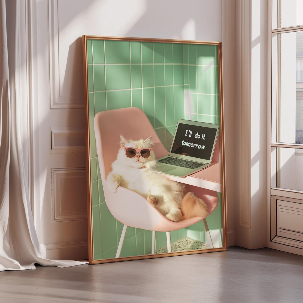A framed image of a cat sitting in a pink chair, wearing sunglasses, and resting its paw on a laptop computer with the text "I'll do it tomorrow" displayed on the screen.