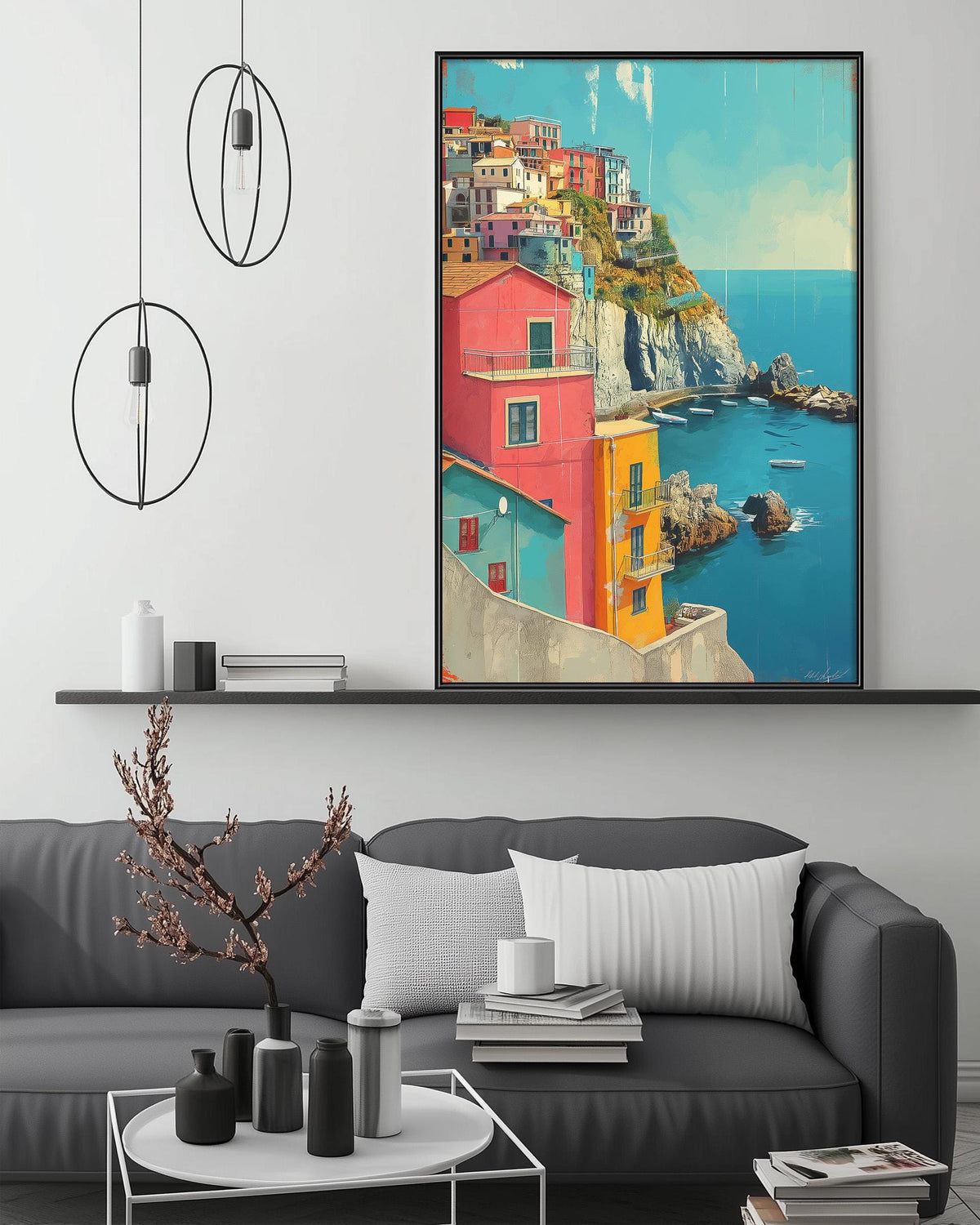 a large, colorful painting of a coastal town with buildings in various shades of pink, orange, and yellow, set against a blue sky and ocean backdrop. The painting is displayed on a wall above a gray couch, which has a coffee table in front of it. The room also includes a shelf with decorative items and a pendant light fixture.