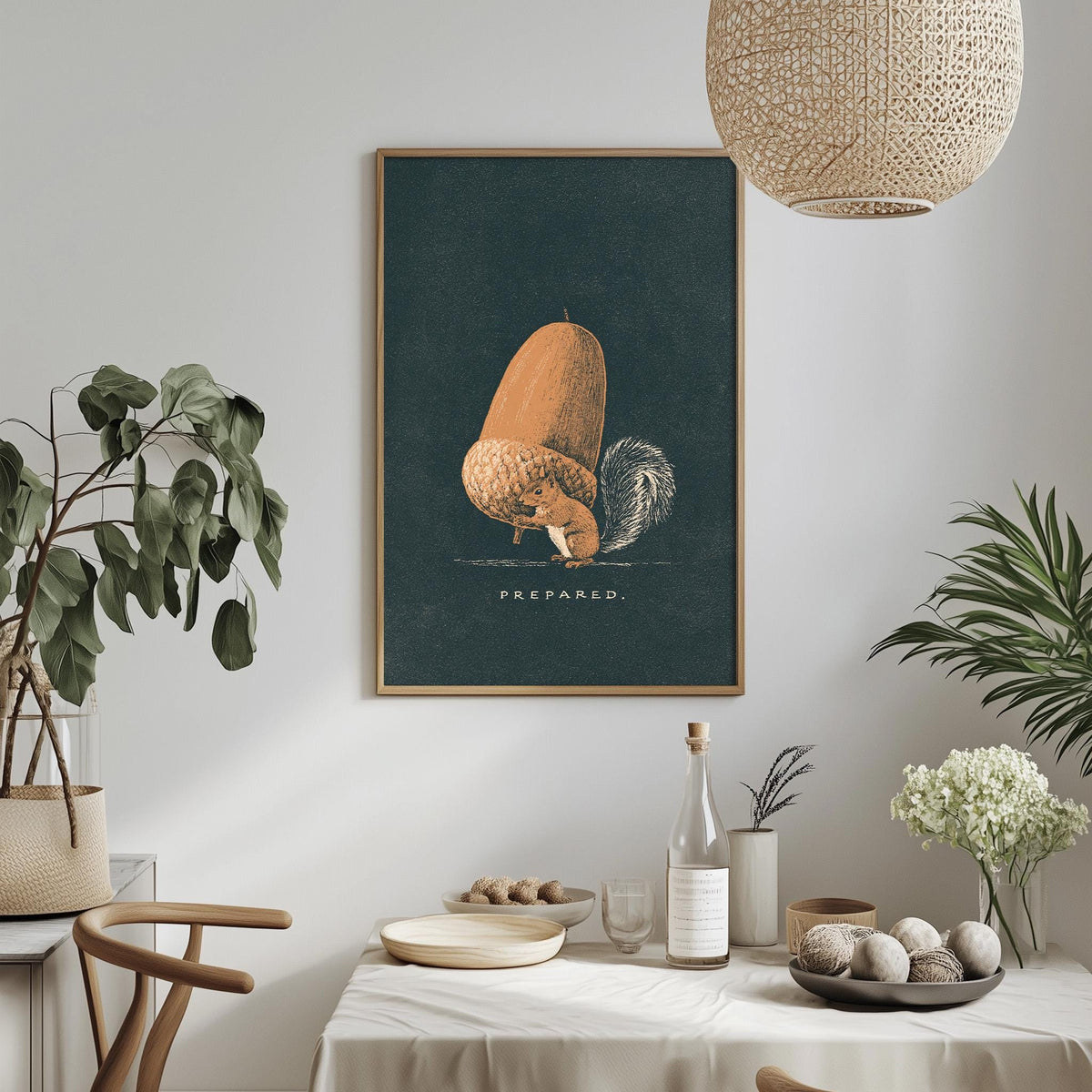 a dining table with a white tablecloth, a bowl of fruit, a bottle, and a vase with flowers. Above the table, there is a framed illustration of an acorn with the word "PREPARED" written on it.