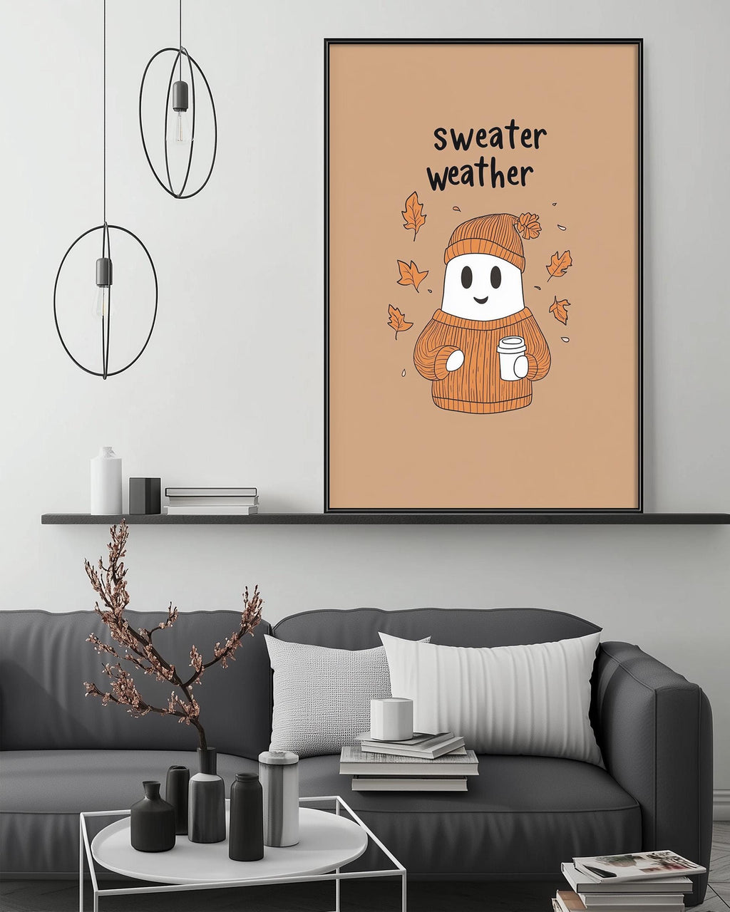 a cozy living room with a gray couch, a coffee table, and a framed poster of a ghost wearing a sweater and holding a cup of coffee. The poster has the text "sweater weather" written on it.