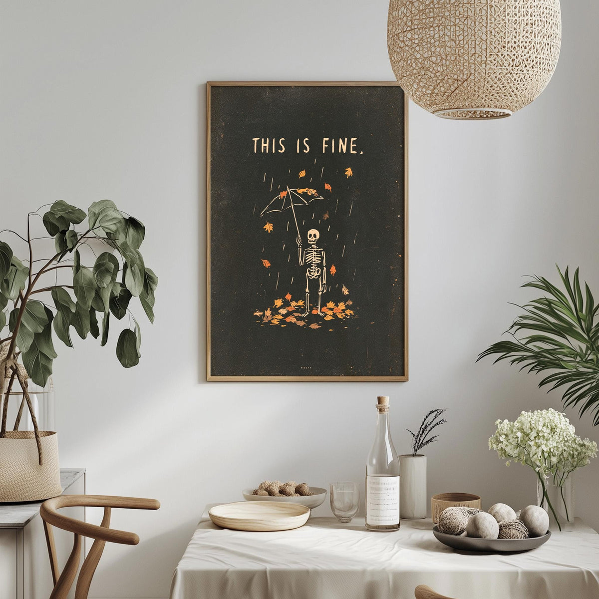 a framed poster with a skeleton holding an umbrella, surrounded by autumn leaves, hanging on a wall above a dining table with various items on it.