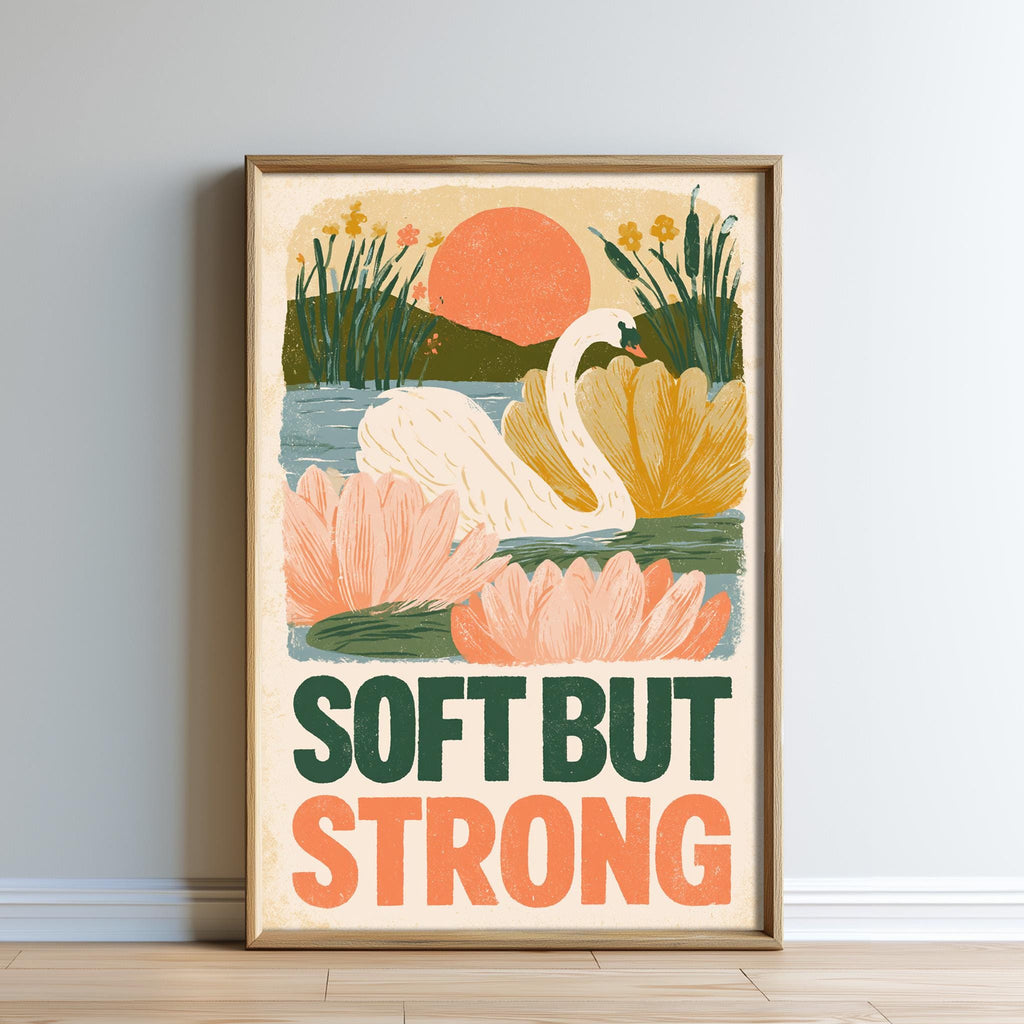 The image is a framed poster with a colorful illustration of a swan, flowers, and a sunset. The text on the poster says "Soft but Strong".