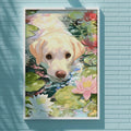 A framed painting of a yellow Labrador retriever dog is hanging on a blue brick wall, surrounded by a variety of colorful flowers.
