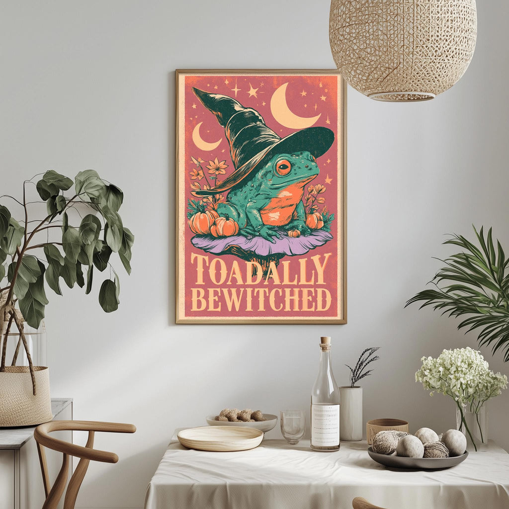 a framed poster of a frog wearing a witch's hat, surrounded by autumn-themed elements such as pumpkins and flowers, with the text "Toadally Bewitched" displayed on the poster.