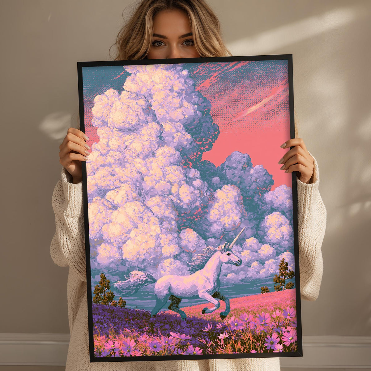 A woman holds up a framed picture of a white unicorn running through a field of flowers, with a pink and blue sky in the background.