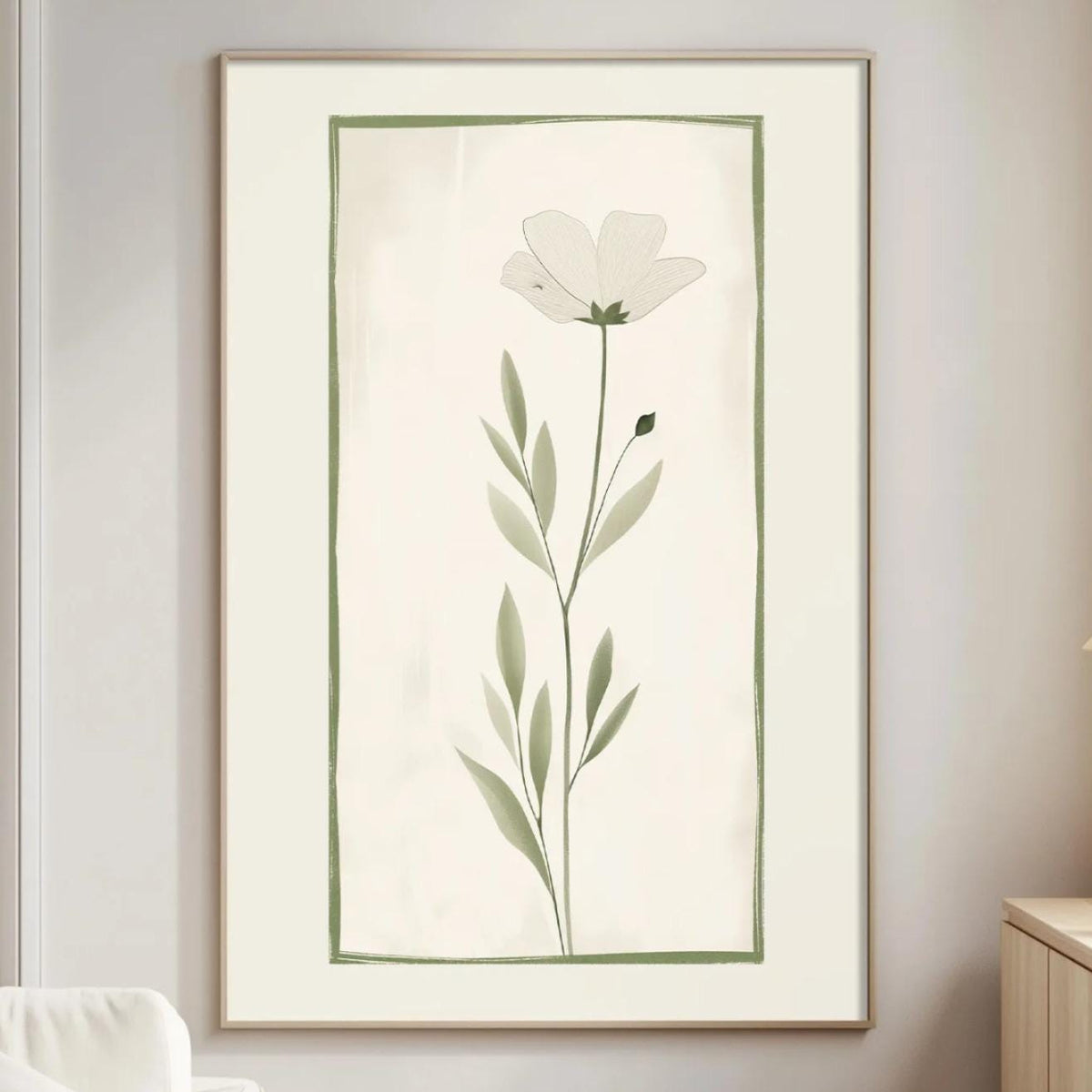 a serene living room with a large framed print of a white flower with green leaves hanging on the wall. The room is furnished with a white sofa, a wooden side table, and a lamp on a wooden cabinet.