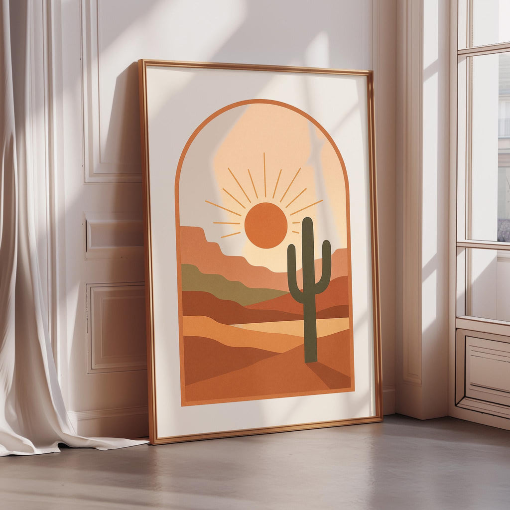 a framed poster of a desert landscape with a cactus in the foreground, set against a warm, orange and yellow background.