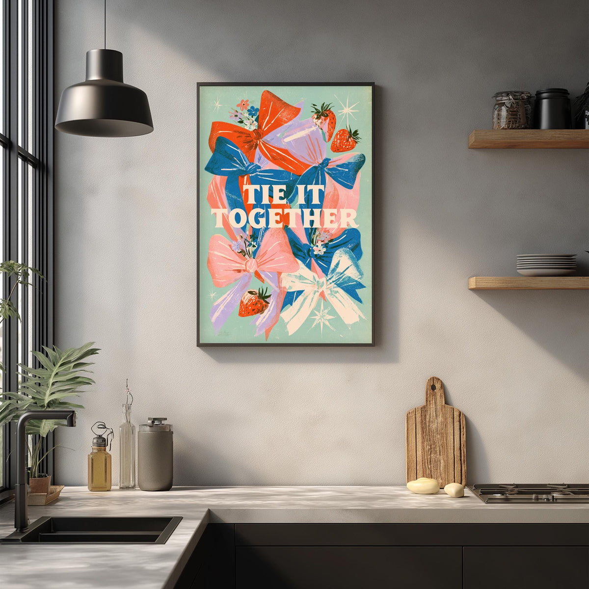 a kitchen counter with various items such as a cutting board, a soap dispenser, and a potted plant. Above the counter, there is a framed poster with the text "TIE IT TOGETHER" and colorful illustrations of flowers and strawberries.