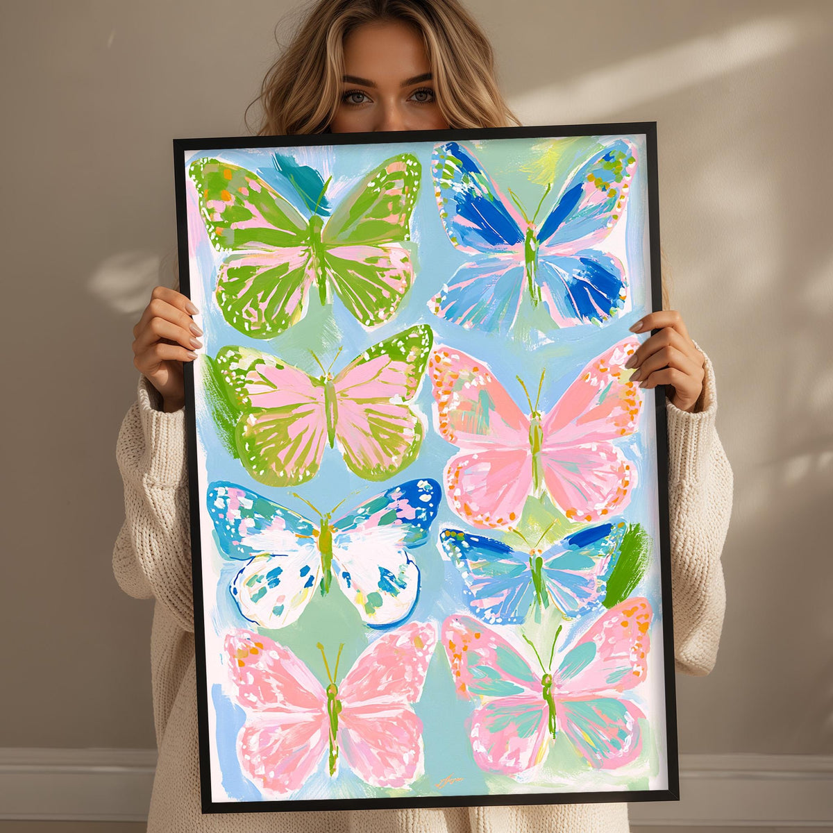 A woman is holding up a framed print of colorful butterflies, displaying a vibrant collection of seven butterflies in various shades of green, pink, blue, and orange.