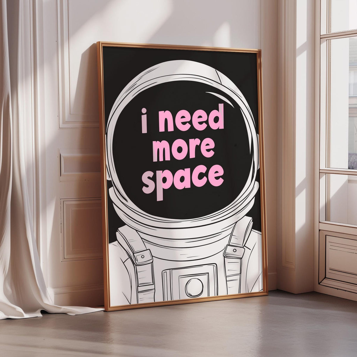 A framed poster with a black background and a white illustration of an astronaut's helmet, displaying the text "I need more space" in pink letters.