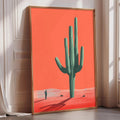 a large framed poster of a cactus against a bright orange background, with a person standing in the foreground.