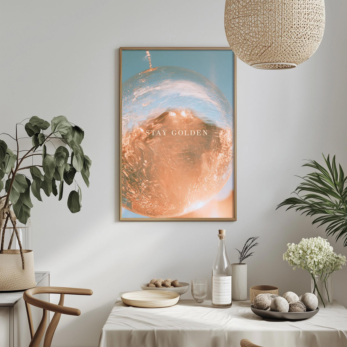 a dining table with a bowl of fruit, a bottle, and a vase of flowers, along with a framed picture hanging on the wall above the table.