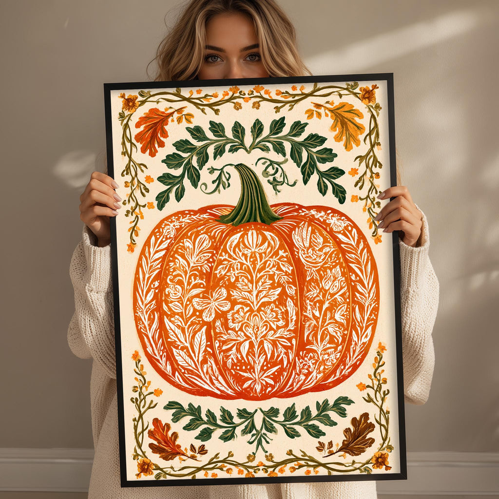 A woman is holding up a framed print with a large pumpkin design on it, surrounded by autumn leaves and flowers.