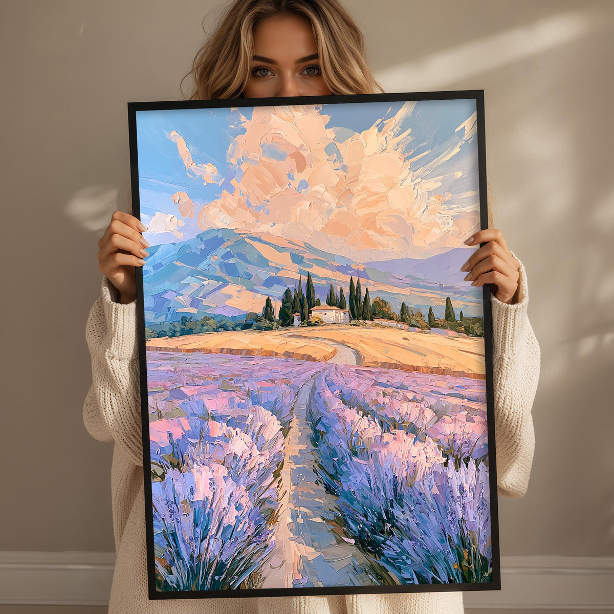 A woman holds up a framed painting of a picturesque landscape with a winding path leading through a field of lavender flowers.