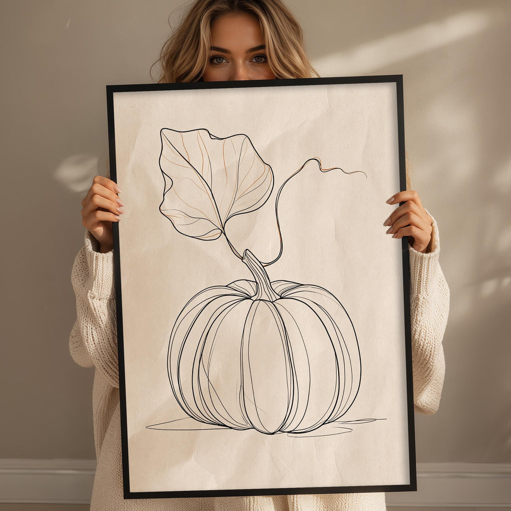 A woman is holding up a framed print of a pumpkin with a leaf on it.