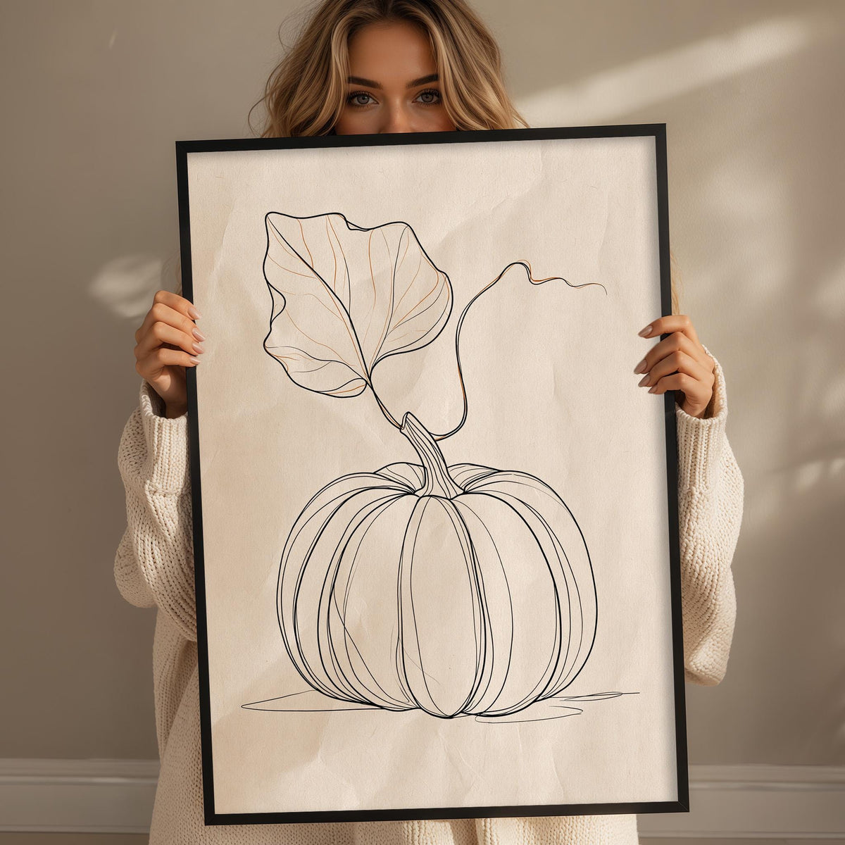 A woman is holding up a framed print of a pumpkin with a leaf on it.