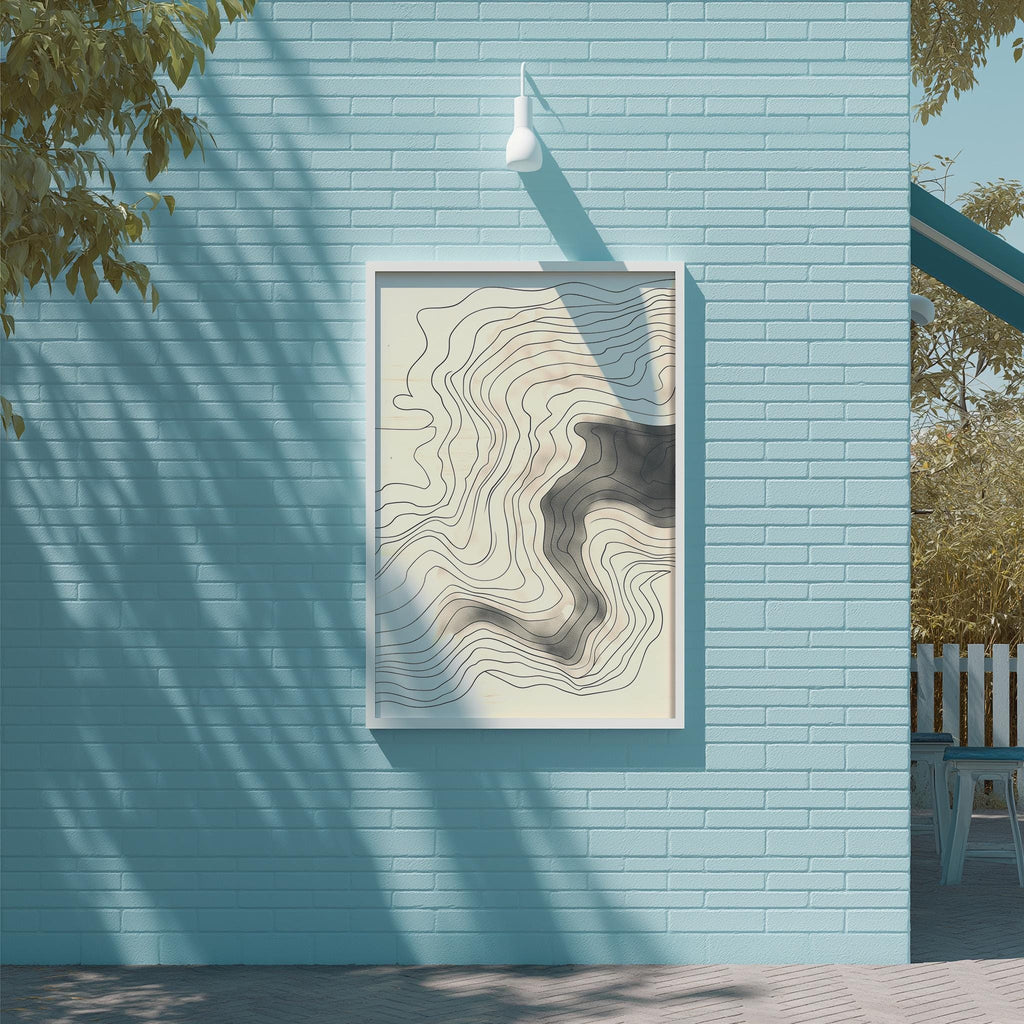 a blue brick wall with a framed abstract artwork hanging on it. The artwork has a wavy, abstract design in shades of gray and white. The wall is situated next to a tree, and there is a white light fixture mounted on the wall.