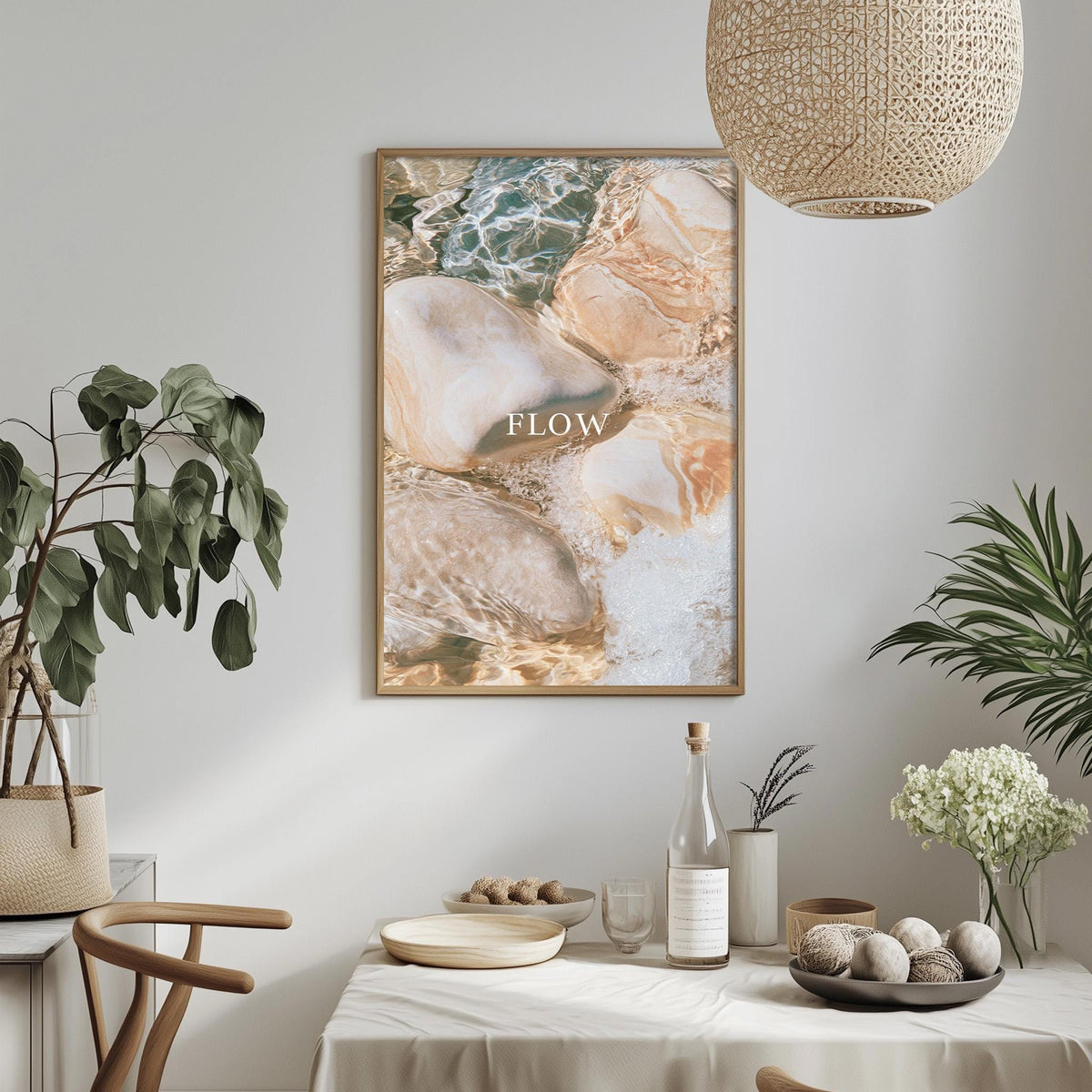 a dining table with a bowl of fruit, a bottle, and a vase of flowers, along with a framed picture hanging on the wall above the table.