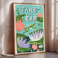 a framed poster with a vibrant illustration of a frog leaping over a pond filled with colorful flowers and plants.