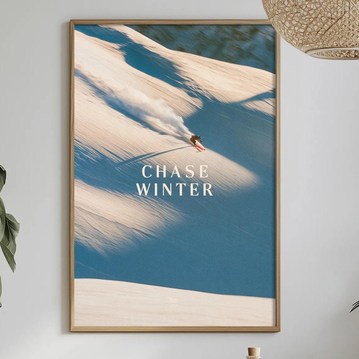 a dining table with a bowl of fruit, a bottle, and a vase of flowers, along with a framed picture of a person skiing on a snowy mountain.