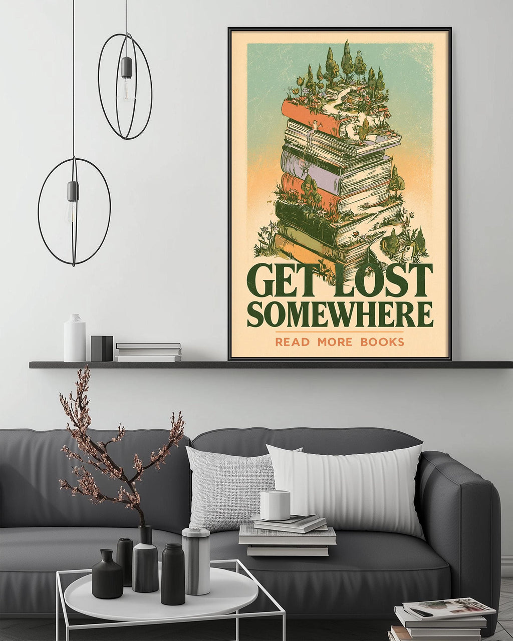 a cozy living room with a gray couch, a coffee table, and a bookshelf filled with books. Above the couch, there is a framed poster with a whimsical illustration of a stack of books surrounded by trees and plants, along with the text "GET LOST SOMEWHERE READ MORE BOOKS".