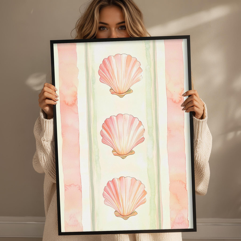 A woman holding a framed picture of three pink seashells.