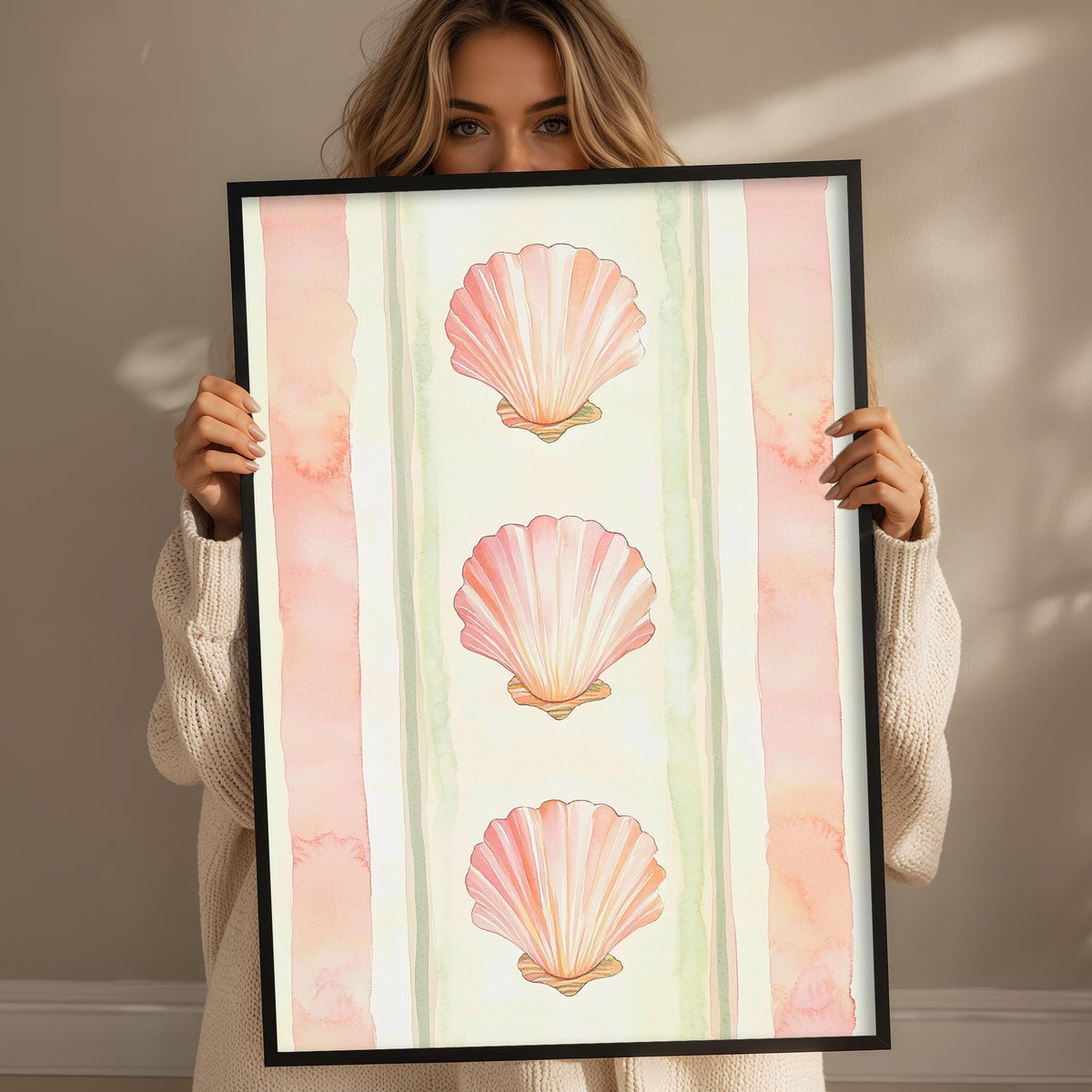A woman holding a framed picture of three pink seashells.