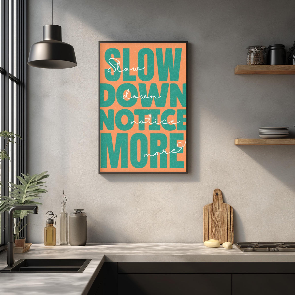 a kitchen counter with a framed poster hanging on the wall above it. The poster has the text "Slow down, notice more" in a large, colorful font.