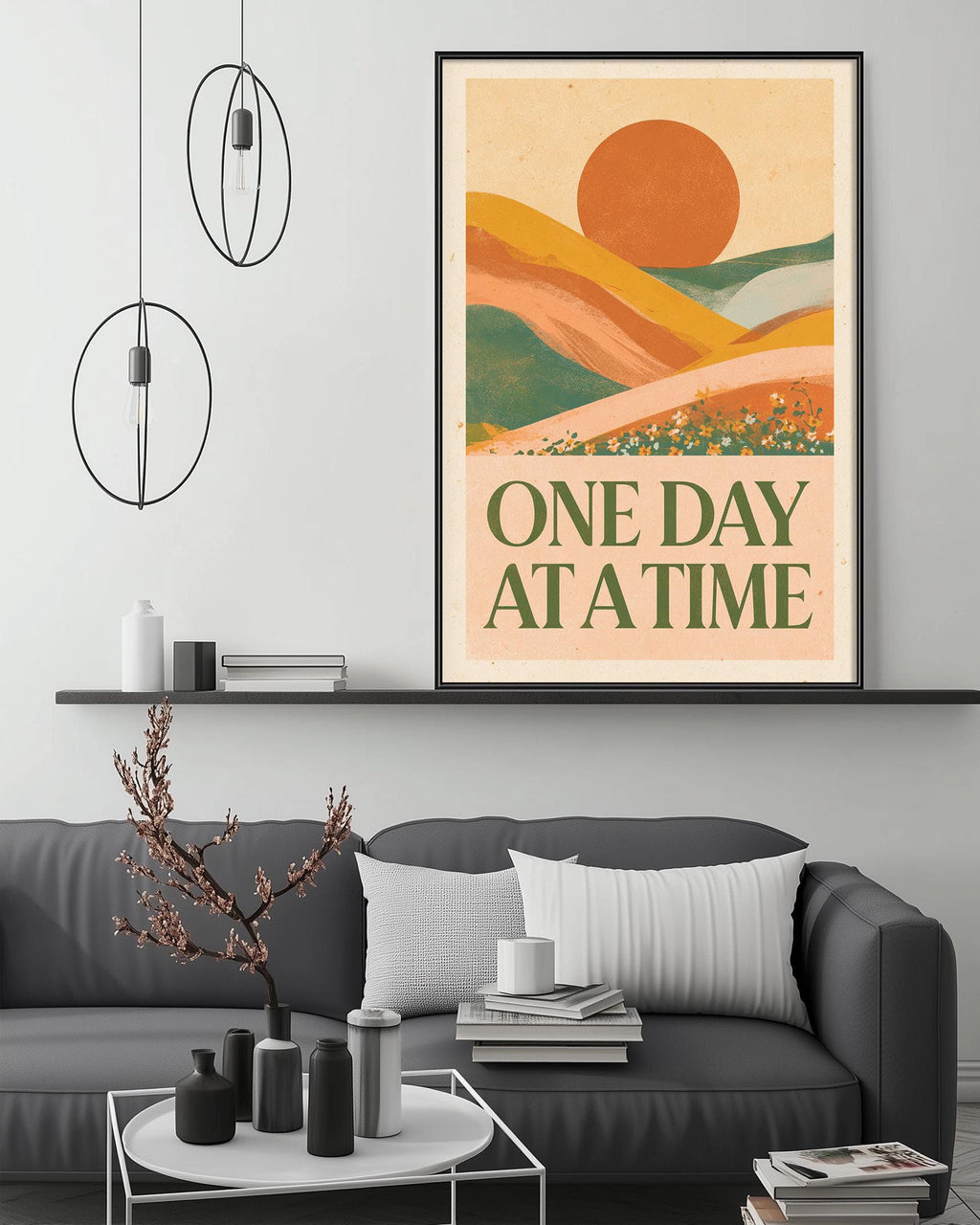 a living room with a gray sofa, a coffee table, and a framed poster on the wall. The poster has a landscape with a sun and mountains, and the text "ONE DAY AT A TIME" is written below the image.