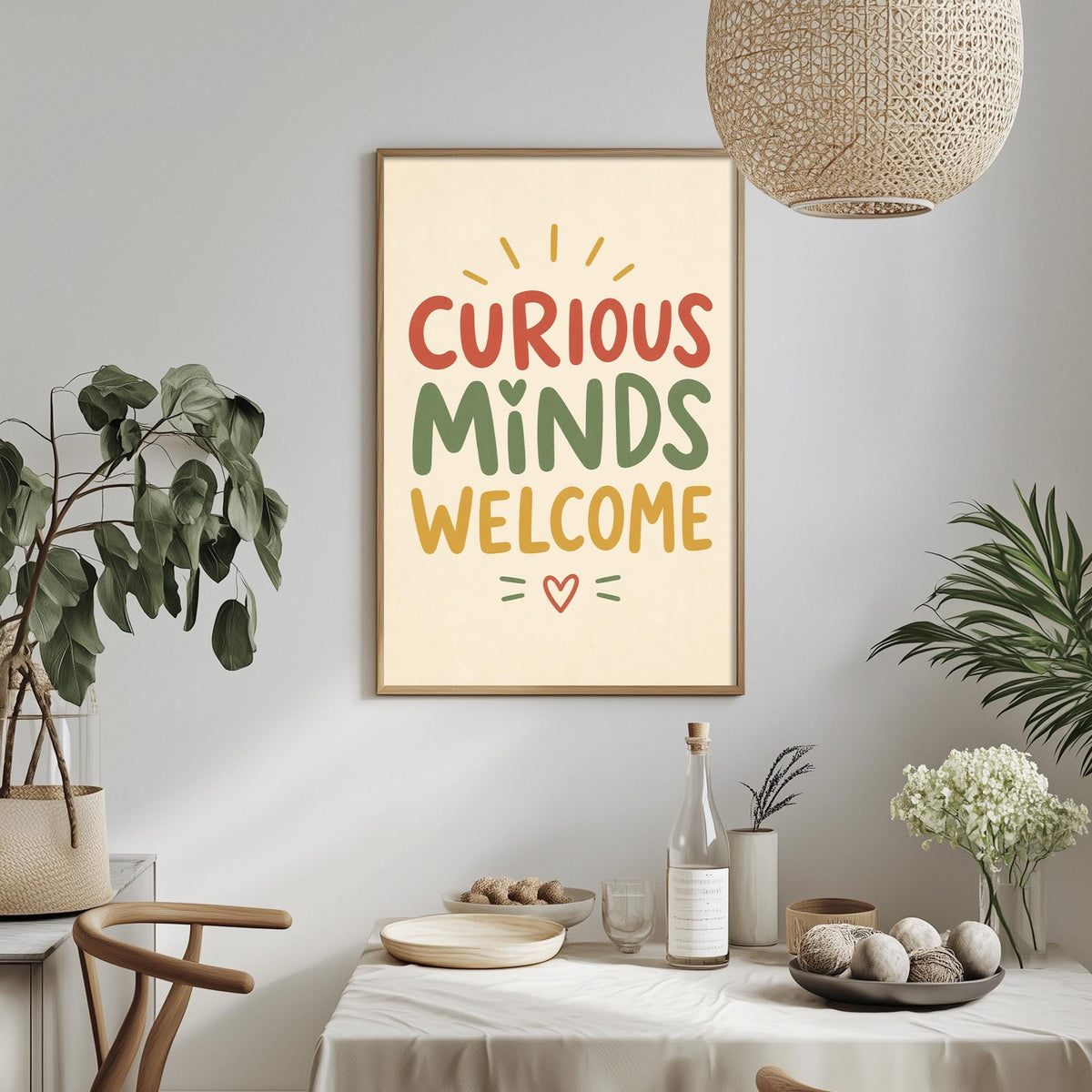 a framed poster with the text "CURIOUS MINDS WELCOME" hanging on a wall above a dining table with various items on it, including a bottle, a bowl, and a vase.