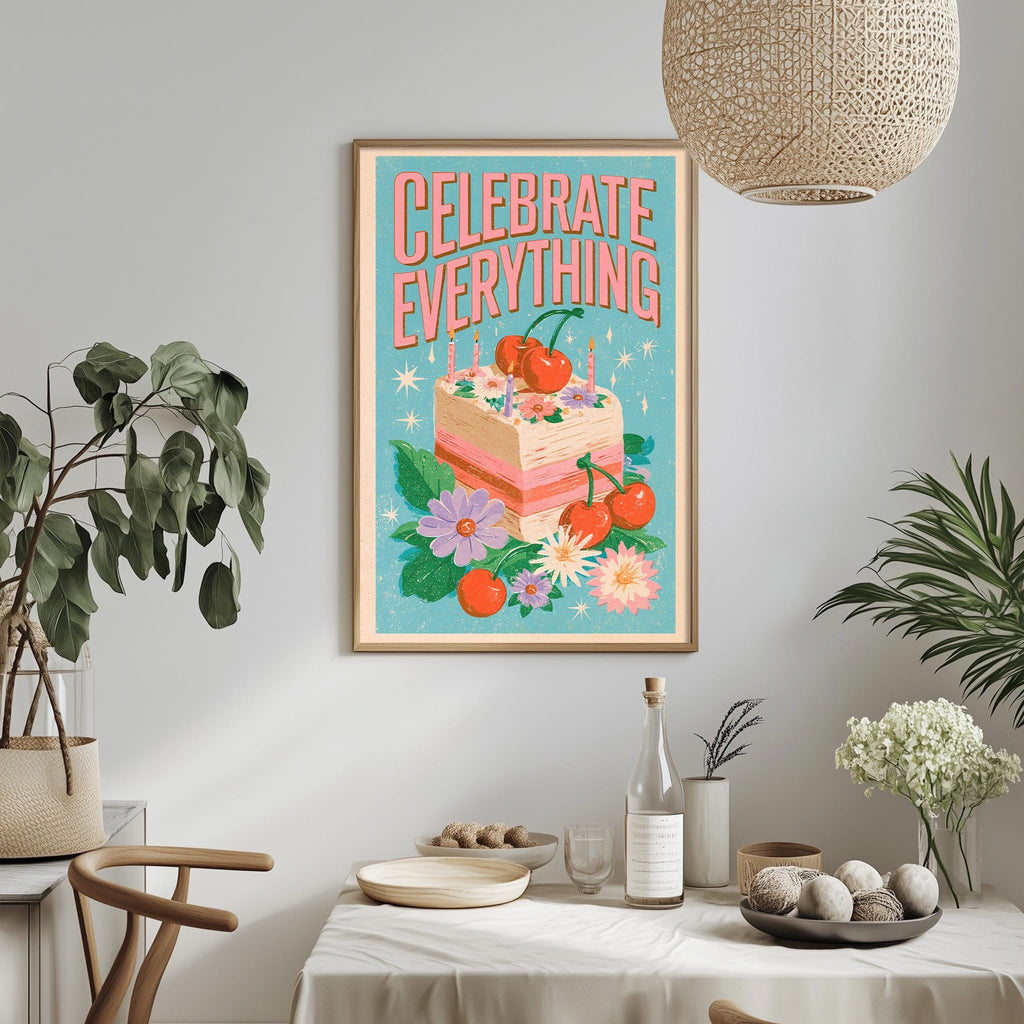 a framed poster with a colorful illustration of a cake surrounded by flowers and plants, along with the text "Celebrate Everything" displayed on the poster. The poster is hanging on a wall above a dining table, which has various items on it, such as a bottle, a bowl, and a vase. The table is set with a white tablecloth and there are some potted plants in the background.