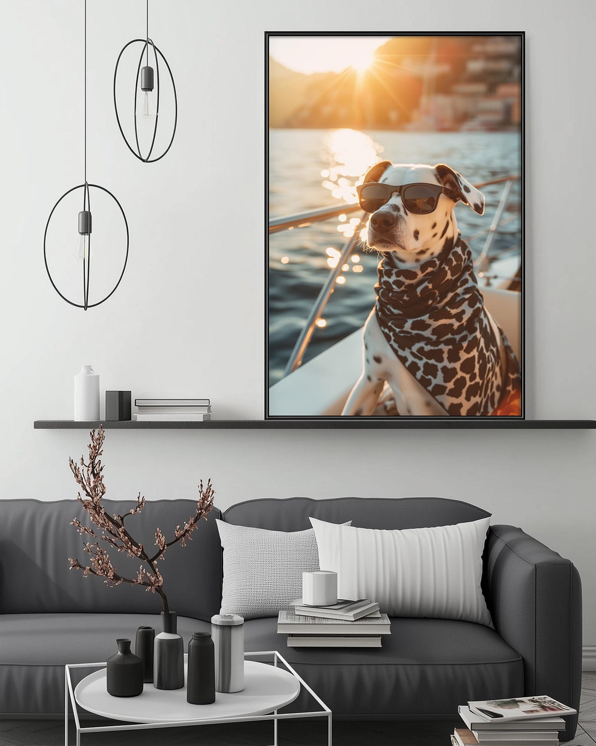 A Dalmatian dog wearing sunglasses is sitting on a boat, with a scenic sunset in the background, as depicted in a framed artwork hanging on the wall above a gray couch in a modern living room setting.