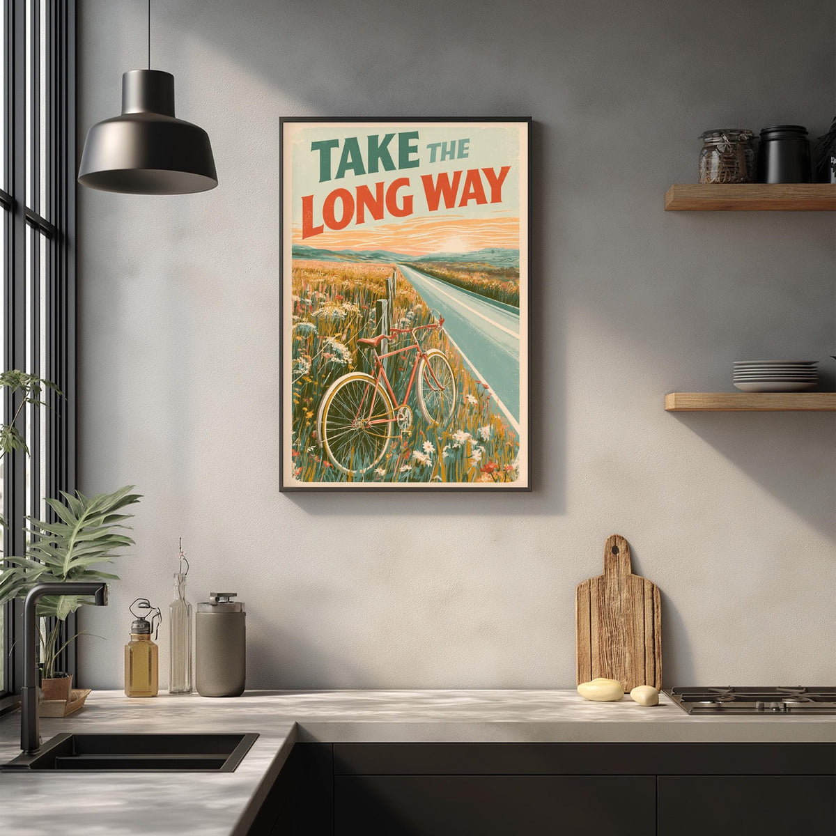 a framed poster with a bicycle and a road, hanging on a wall above a kitchen counter with various kitchen items and a cutting board.
