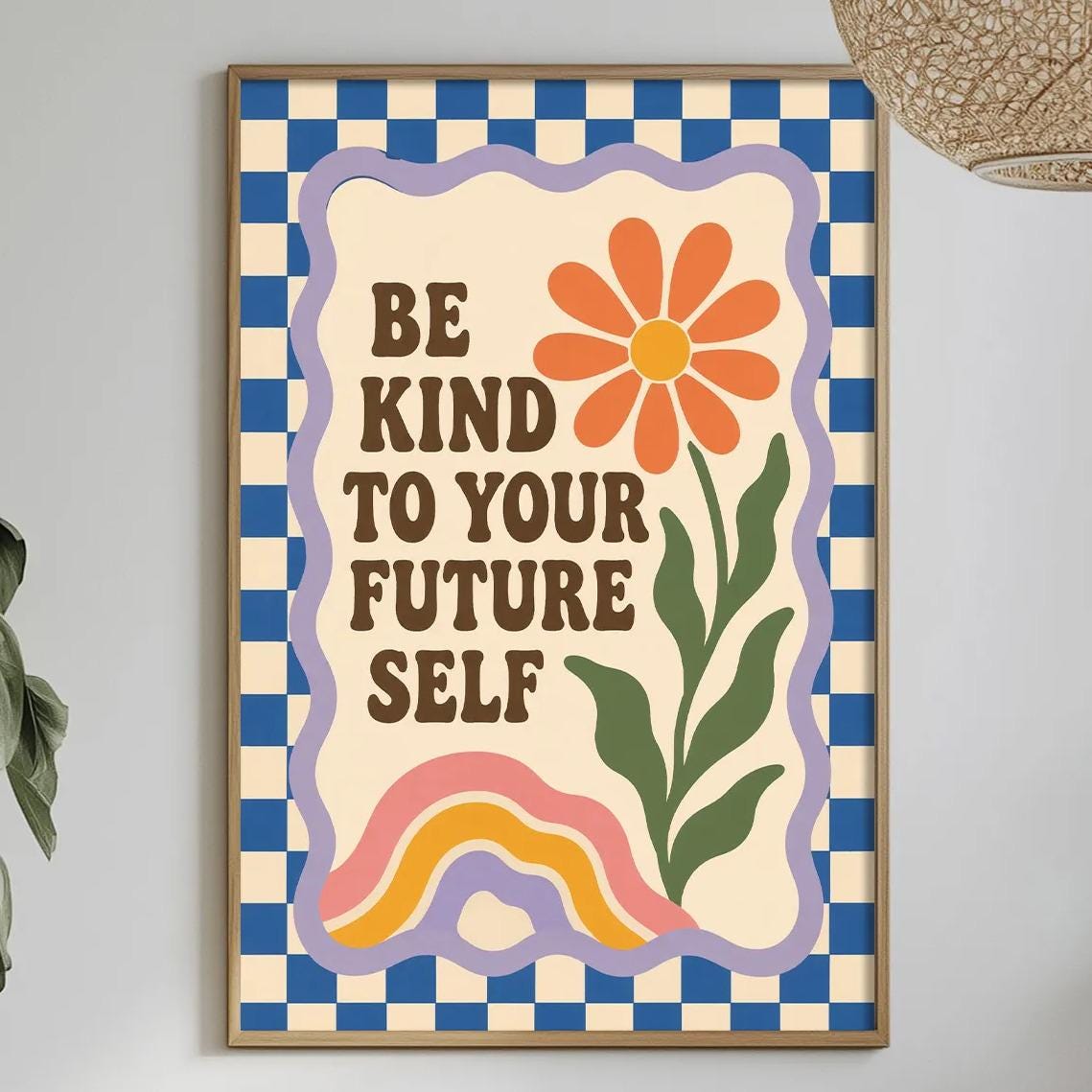 a framed poster with the text "Be kind to your future self" and a flower design, hanging on a wall above a dining table with various items on it.