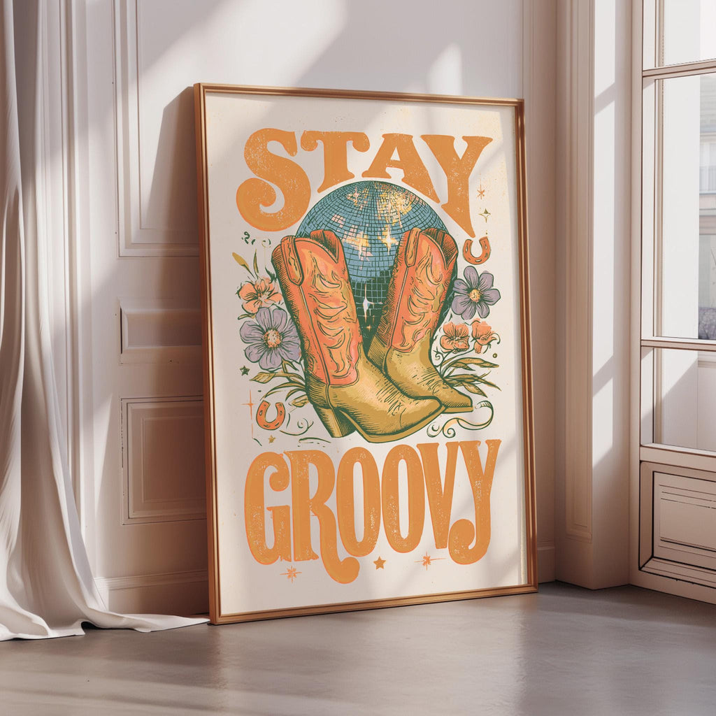 A framed poster with the text "STAY GROOVY" and an illustration of a pair of cowboy boots, a disco ball, and flowers.