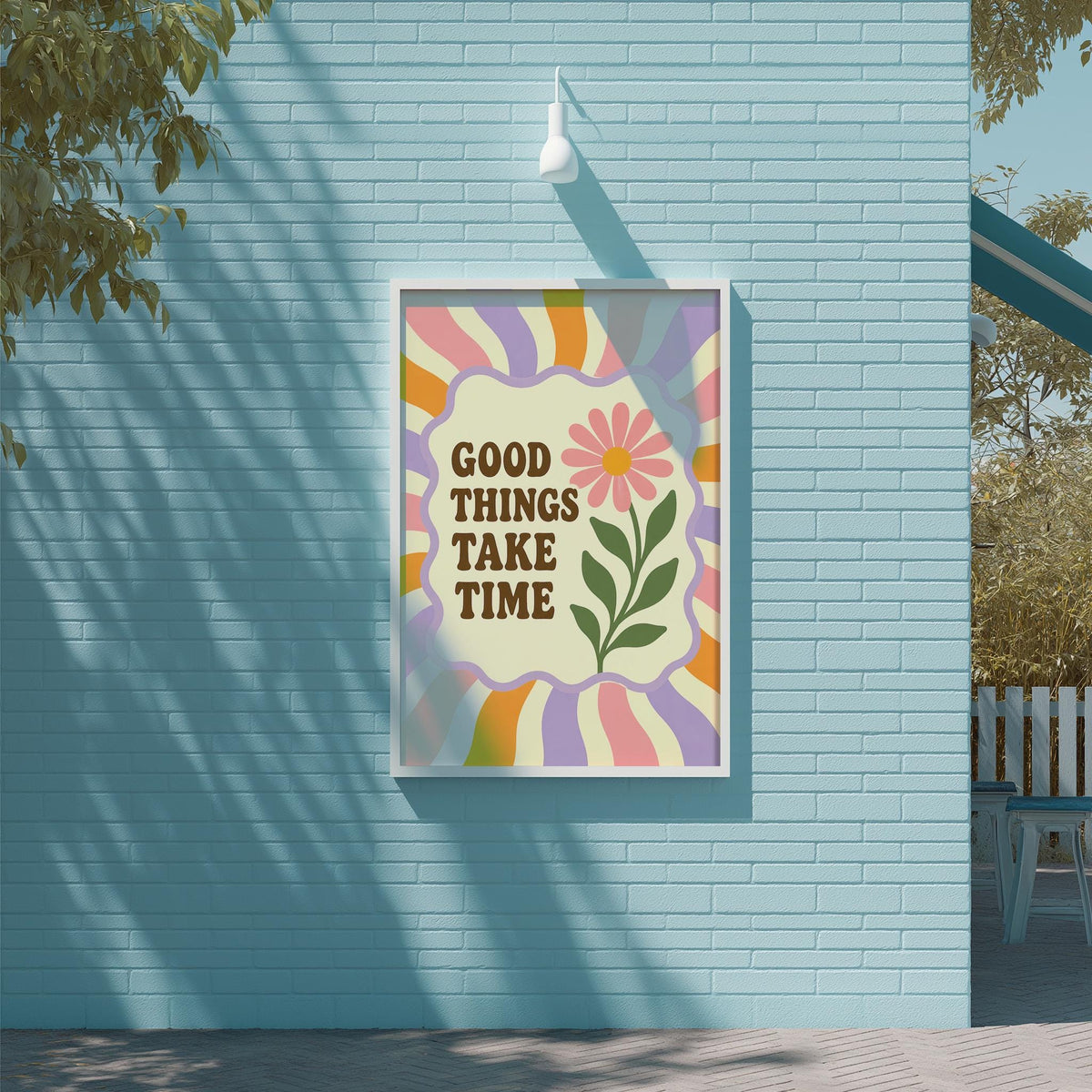 A framed poster with the text "GOOD THINGS TAKE TIME" is displayed on a blue brick wall, with a tree and a white light fixture visible in the background.